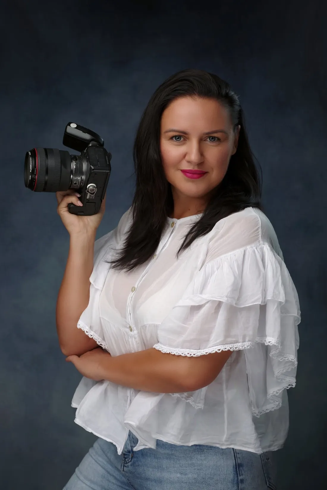 Magda Suszka-Krawiec w białej bluzce z aparatem Canon w dłoni, portret w studiu.